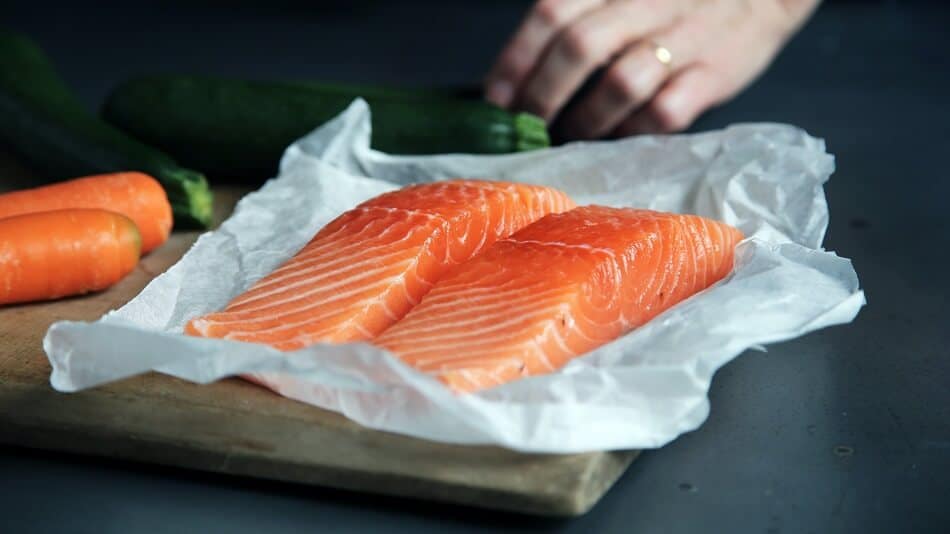 Two Thick Slices of Raw Salmon on a Wooden Board with Carrots and Cucumber