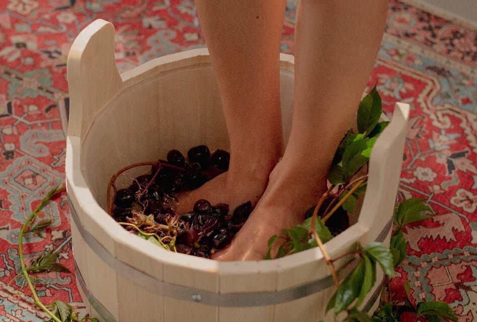 Woman Steps into Wooden Container to Crush Grapes with Their Feet